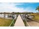 A wooden dock extends over the lake towards a boat lift and covered dock, framed by lush landscaping at 1007 143Rd Ne St, Bradenton, FL 34212