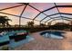 A screened pool area features a pool with a hot tub, fire table, and outdoor seating under a colorful sunset sky at 3814 Scrub Creek Run, Lakewood Ranch, FL 34211