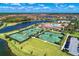 Aerial view of a community's tennis courts, a lake, and surrounding homes amidst lush landscaping at 19889 Benissimo Dr, Venice, FL 34293