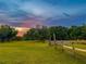 A tranquil pasture scene with a wooden fence, grazing deer, and a backdrop of lush trees under a colorful sunset sky at 1208 Oak Hammock Rd, Sarasota, FL 34240