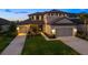 Charming two-story home featuring a manicured lawn and a three-car garage with individual doors at twilight at 16626 Paynes Mill Dr, Lakewood Ranch, FL 34211