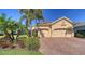 Charming home featuring a brick driveway, two-car garage, and lush tropical landscaping with palm trees at 21287 Sandal Foot Dr, Venice, FL 34293