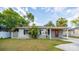 Quaint single-story home with a red door and a covered porch, surrounded by lush greenery and a well-kept lawn at 3515 W Pearl Ave, Tampa, FL 33611