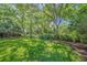 Spacious backyard with vibrant green lawn, mature trees, and manicured landscaping offers serenity and privacy at 6390 Yellow Wood Pl, Sarasota, FL 34241
