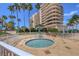 A secluded hot tub surrounded by a white fence and greenery is set against a high rise building and palm trees at 3030 Grand Bay Blvd # 323, Longboat Key, FL 34228