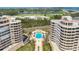 Aerial view features the community pool area nestled between condominium towers, overlooking a golf course and water at 3030 Grand Bay Blvd # 323, Longboat Key, FL 34228