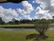 Lush backyard featuring a serene pond, vibrant green grass, and mature trees under a bright blue sky at 5630 Golf Pointe Dr # 108, Sarasota, FL 34243