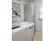 Bright laundry room features white washer and dryer with gray storage cabinets and boat-themed artwork at 5630 Golf Pointe Dr # 108, Sarasota, FL 34243