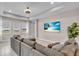 Bright living room featuring a large gray sectional sofa, tray ceiling, a beach-themed wall-mounted television, and natural light at 17502 Savory Mist Cir, Bradenton, FL 34211