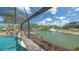 Breathtaking waterfront view of a pool with a waterfall, dock, and lush landscaping within a screened enclosure at 452 Picasso Dr, Nokomis, FL 34275