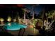 Relaxing poolside patio with chairs and table, surrounded by lush, illuminated landscaping at night at 606 Emerald Ln, Holmes Beach, FL 34217