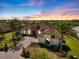 Stunning aerial view of a single-Gathering home with lush landscaping, brick driveway, and barrel tile roof at sunset at 26725 Raphis Royale Blvd, Englewood, FL 34223