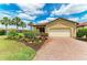 Inviting home with a brick driveway, two-car garage, lush landscaping, and beautiful palm trees against a bright sky at 10111 Malachite Dr, Bradenton, FL 34211