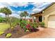 Charming home showcasing a brick driveway, manicured flower beds, and tropical palm trees against a partly cloudy sky at 10111 Malachite Dr, Bradenton, FL 34211