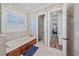 Spa-like bathroom with a soaking tub, wood cabinets, tiled walls, and open doorway to the hall at 6600 Horned Owl Pl, Sarasota, FL 34241
