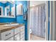 Bright blue bathroom features a white vanity with a tan countertop and blue and white patterned shower curtain at 9011 Hilolo Ln, Venice, FL 34293