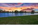Scenic view of a calm lake reflecting a vibrant sunset, framed by lush green grass at 10217 Canaveral Cir, Sarasota, FL 34241