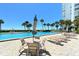 Chairs and table beside a community pool with a white high-rise building and ocean in the background on a clear and sunny day at 1050 Longboat Club Road # 903, Longboat Key, FL 34228