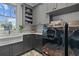Laundry room with open shelving, gray cabinets, farmhouse sink, white countertops, and modern, black washing machine at 12615 River Rd, Myakka City, FL 34251