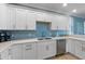 This kitchen features white cabinets, stainless steel dishwasher, and a complementary blue backsplash at 306 Poinsettia Rd, Anna Maria, FL 34216
