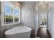 Bright bathroom featuring a soaking tub beneath a window with stylish light fixture, and a view into the bedroom at 8223 Snowy Egret Pl, Bradenton, FL 34202