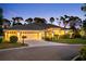 Exterior elevation view of house featuring a three car garage, tile roof and landscaped lawn at dusk at 2196 Muskogee Trl, Nokomis, FL 34275