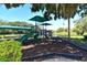 Community playground with slides, climbing structures, and covered areas, set against a backdrop of lush trees and a tranquil pond at 5032 Timber Chase Way, Sarasota, FL 34238