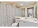 Well-lit bathroom features large mirror over a white vanity and toilet with grey curtained shower at 6209 Erice St, Venice, FL 34293