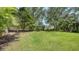 Large backyard with healthy green grass, mature trees, bushes, and a partial fence line at 7158 Westhill Ct, Lakewood Ranch, FL 34202