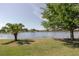 A tranquil lakefront view framed by mature trees and lush green grass creates a serene backyard setting at 12740 Del Corso Loop, Lakewood Ranch, FL 34211