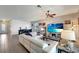 Bright living room with a white leather sofa, ceiling fan, and television with beach image at 15719 Barefoot Beach Dr, Lakewood Ranch, FL 34211