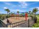 Community playground with swings, slides, and play structures surrounded by a secure fence and lush landscaping at 15719 Barefoot Beach Dr, Lakewood Ranch, FL 34211