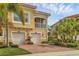 Inviting yellow townhouse featuring dual garages, red brick driveway, lush landscaping, and a charming second-story screened balcony at 4236 Expedition Way # 106, Osprey, FL 34229