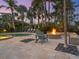 Resort-style backyard with heated pool, cozy firepit, travertine pavers, mature palm trees, and comfortable Adirondack chairs at 497 Island Cir, Sarasota, FL 34242