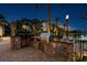 Beautiful outdoor kitchen with stone surround, stainless grill, and granite counters, overlooking a lake at twilight at 12224 Garden Lake Cir, Odessa, FL 33556
