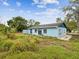 A light blue single-story home is shown, featuring a fenced backyard and lots of green space at 13241 Miami St, Hudson, FL 34667