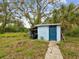 A shed with a blue door and siding is surrounded by lush greenery and a walkway at 13241 Miami St, Hudson, FL 34667