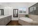 Bright bathroom with grey cabinets, wood-look tile floors and free-standing tub with tiled surround at 4712 Margutta Ct, Sarasota, FL 34240