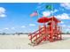 Lifeguard station on the beach with American flag, green flag, umbrella, blue sky, and scattered beachgoers at 2551 Waneta Dr, Sarasota, FL 34231