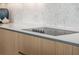 Close-up of a modern kitchen cooktop, white countertops, and stylish wooden cabinetry at 301 Quay Commons # 507, Sarasota, FL 34236