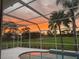 Screened pool with open view of a golf course and orange sunset behind silhouette of trees and palms at 4487 Glebe Farm Rd, Sarasota, FL 34235