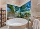 A modern garden tub with a view of tropical plants and palm trees through a large window at 8687 Woodbriar Dr, Sarasota, FL 34238