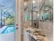 A modern powder room with marble countertops, a frameless mirror, and a view of the pool area at 8687 Woodbriar Dr, Sarasota, FL 34238