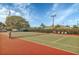 Community tennis court featuring a green and red surface, net, and seating under a sunny sky, trees in the background at 3251 Beneva Rd # 104, Sarasota, FL 34232
