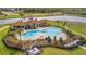 Aerial view of a large community pool, complete with lounge chairs, a splash pad, and lush landscaping at 16341 Little Garden Dr, Wimauma, FL 33598