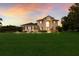 Elegant two-story home with manicured lawn, portico entry and large windows, bathed in the glow of a sunset sky at 3607 Twin Rivers Trl, Parrish, FL 34219