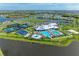 Stunning aerial view of a resort-style community featuring a pool, clubhouse, tennis courts, and lush landscaping by the lake at 15503 Sunny Day Dr, Bradenton, FL 34211