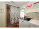 Bright laundry room leading to a shower features modern washer and dryer with storage shelves and tiled shower at 230 47Th W St, Bradenton, FL 34209