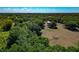 Expansive aerial view of lush, tree-filled acreage with a barn and fenced pasture under a bright blue sky at 4876 253Rd E St, Myakka City, FL 34251