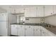 Kitchen area with white cabinetry and appliances; tile backsplash, and view into a small dining area at 600 Sutton Pl # B305, Longboat Key, FL 34228